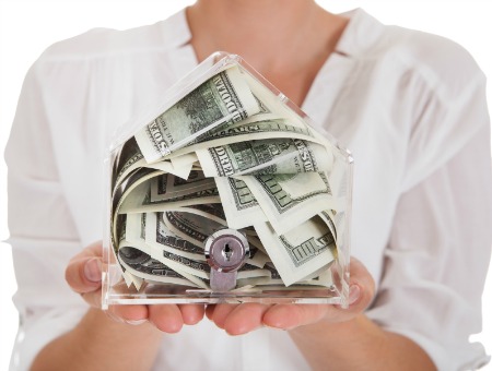 woman holding money in house-shaped box